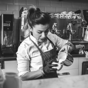 A woman making coffee at a coffee shop dealing with both racial and gender wage gaps.